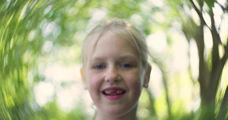 A young girl smiling with a swirling motion blur effect in a lush green setting