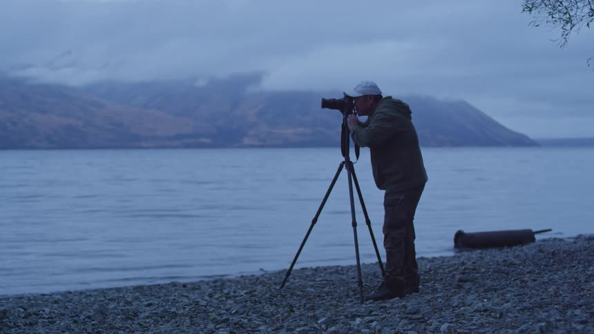 Male photographer using a camera on a tripod by a lake
