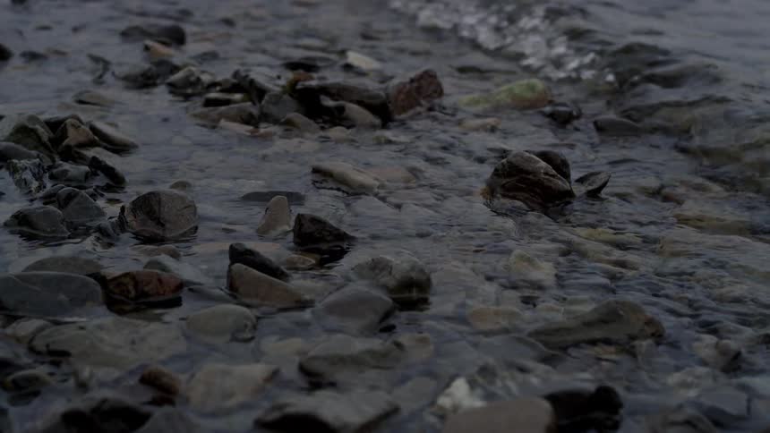Clear water gently rolls over rocks at the waters edge just after sunset before dark