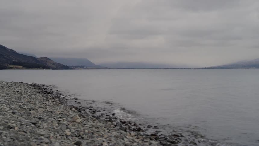 Low waves roll onto a stone covered shore on an overcast day