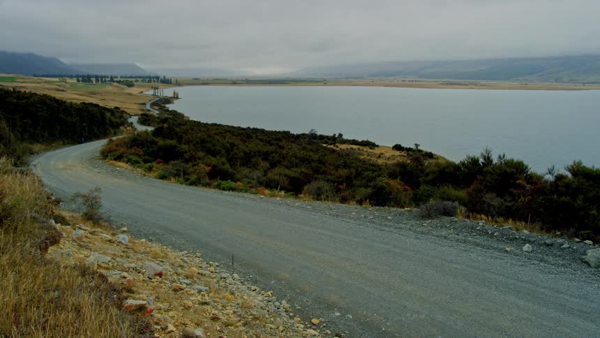 Empty road curves around a lake leading to the mountains on a cloudy day
