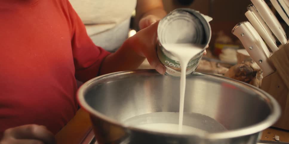 Boy pouring white coconut liquid into a bowl next to his mother