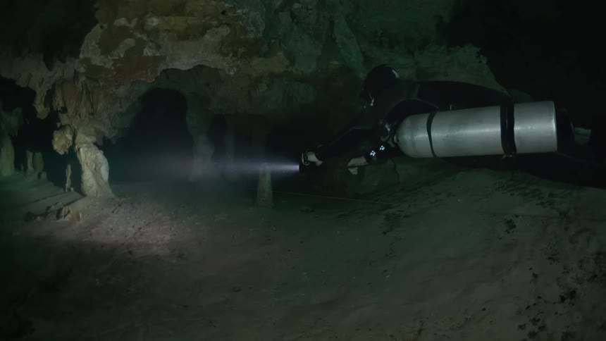 Diver using a flashlight swimming in an underwater cave