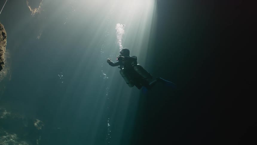A person with diving equipment underwater where sunlight is coming from above
