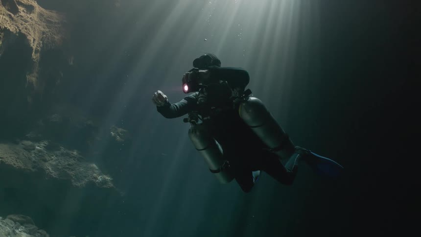 A scuba diver shines a light on the cave rock wall