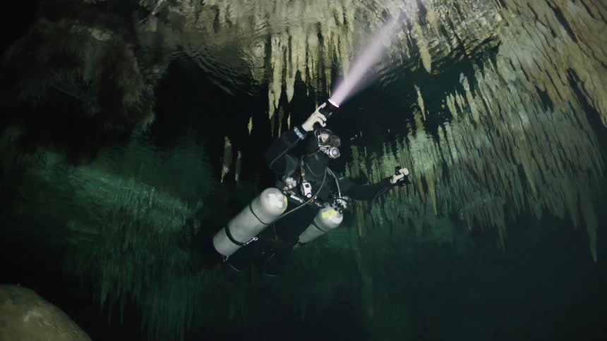 Diver exploring an underwater cave with a flashlight illuminating the stalactites