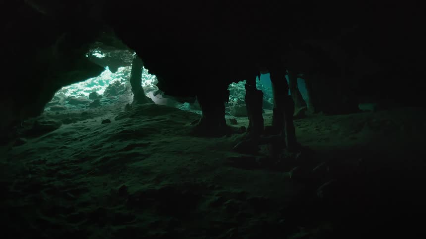 A dark underwater cave illuminated by a distant light source highlighting rock formations and columns