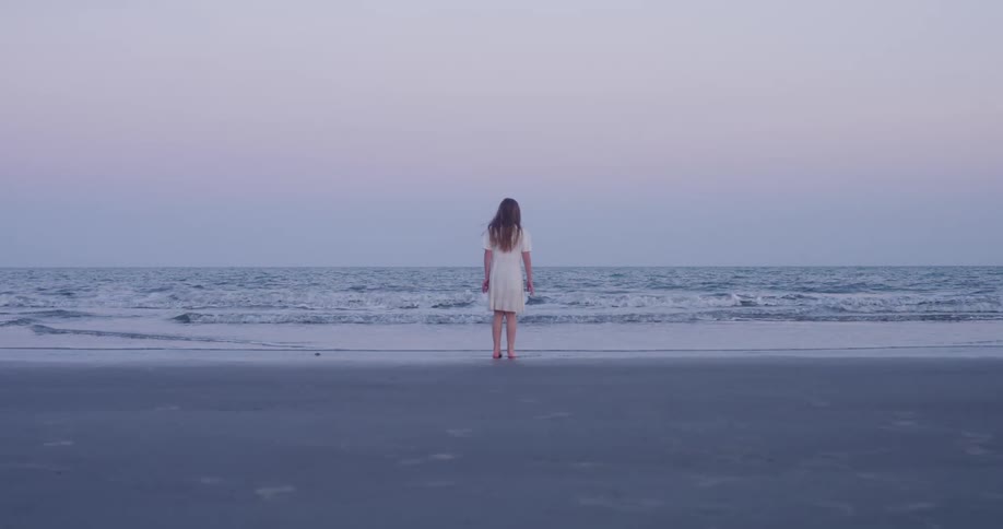 Girl standing on the beach moves her feet as waves roll into shore