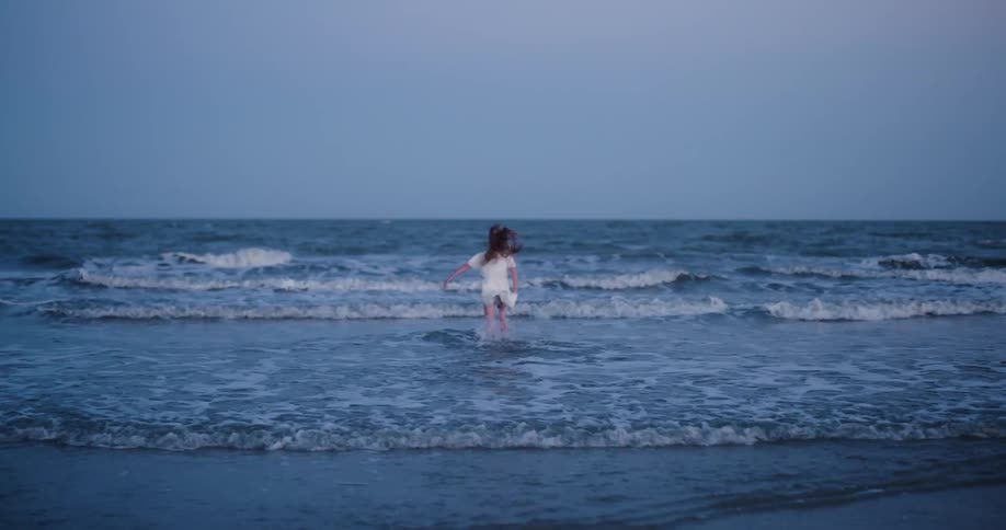 Little girl jumping and running in the waves at the beach