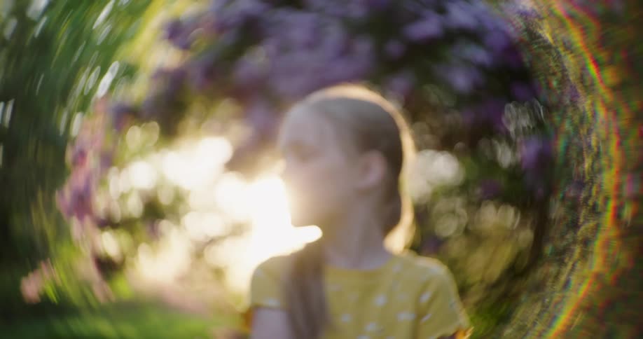 A young girl standing outdoors surrounded by greenery and sunlight