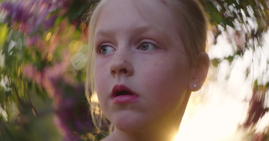 Blonde girl standing outdoors on a sunny day turns her head to look