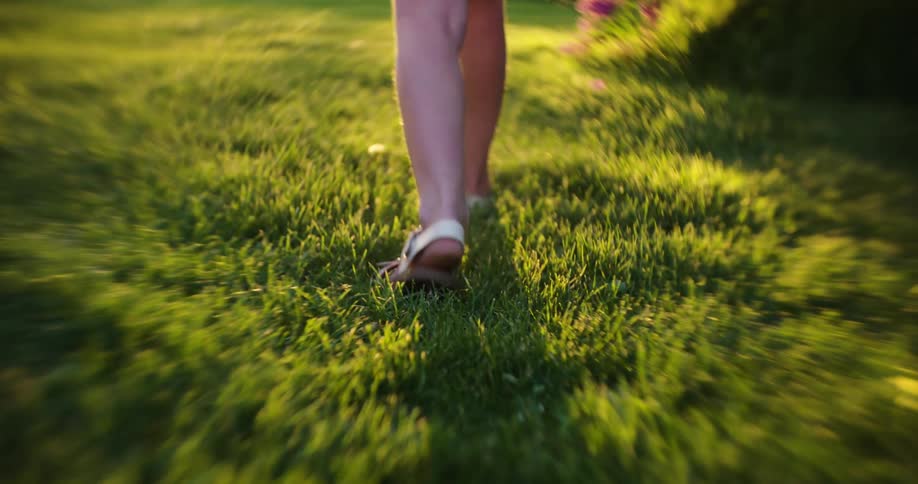 Feet of a child walking on grass and a strong reflection of sunlight