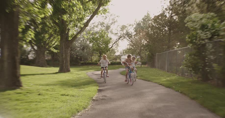 Young girls riding their bikes on a path through a park on a sunny day