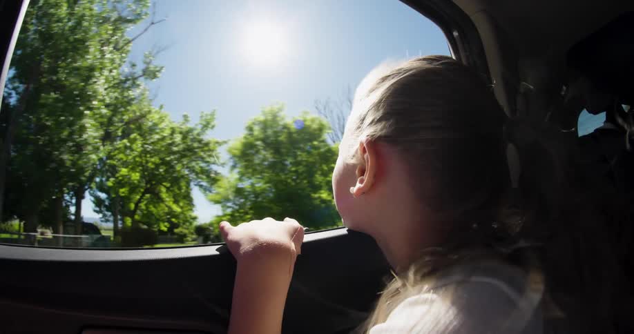 Little girl with the window open getting wind in her face in a moving car
