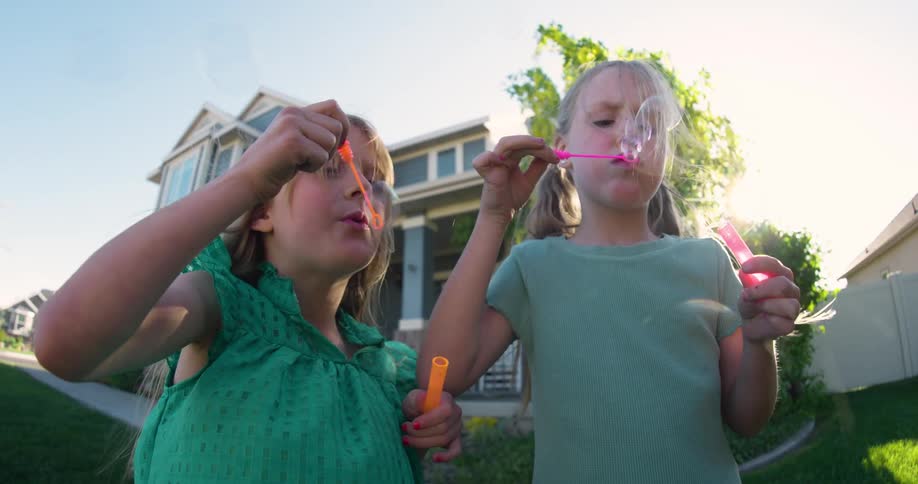 Female friends bubbles while standing in the front yard on a sunny day