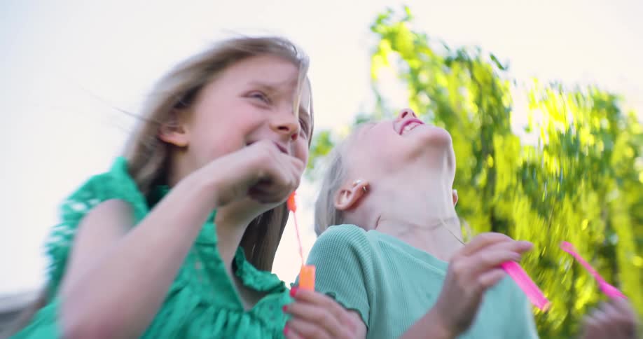 Two little blond children playing with soap bubbles smiling