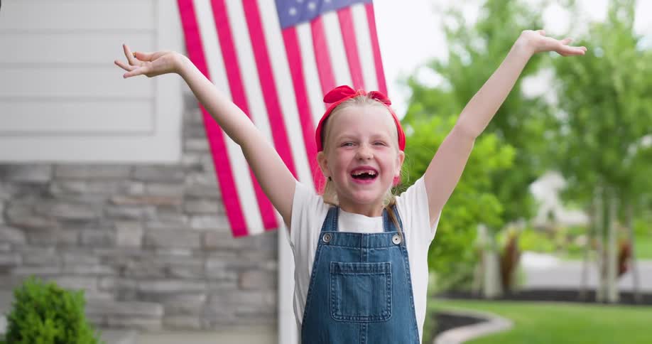 A child raises her arms and cheers with the USA flag in the background