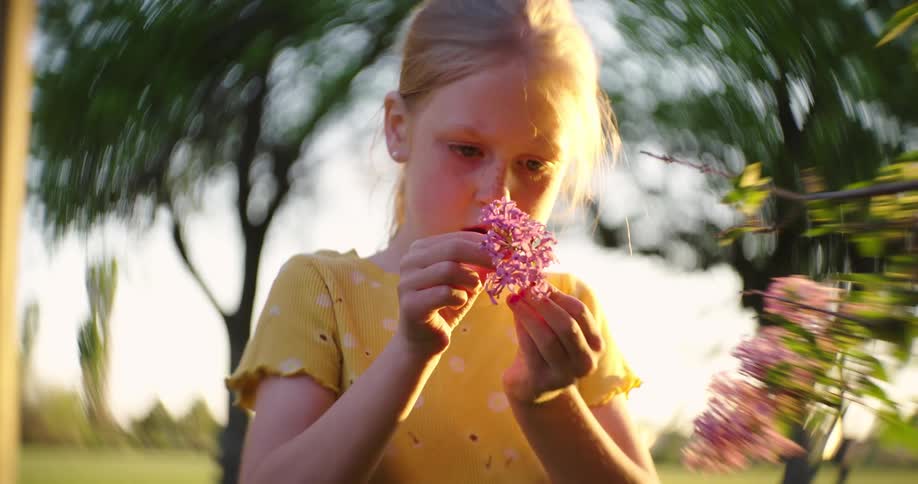 A young girl pulls apart a bunch of small flowers while standing outside