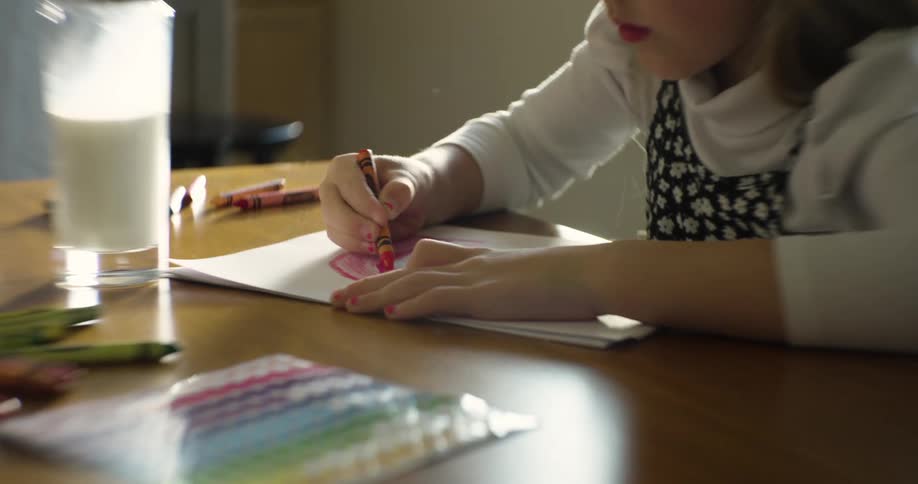 Young girl concentrates while coloring at the table near a glass of milk