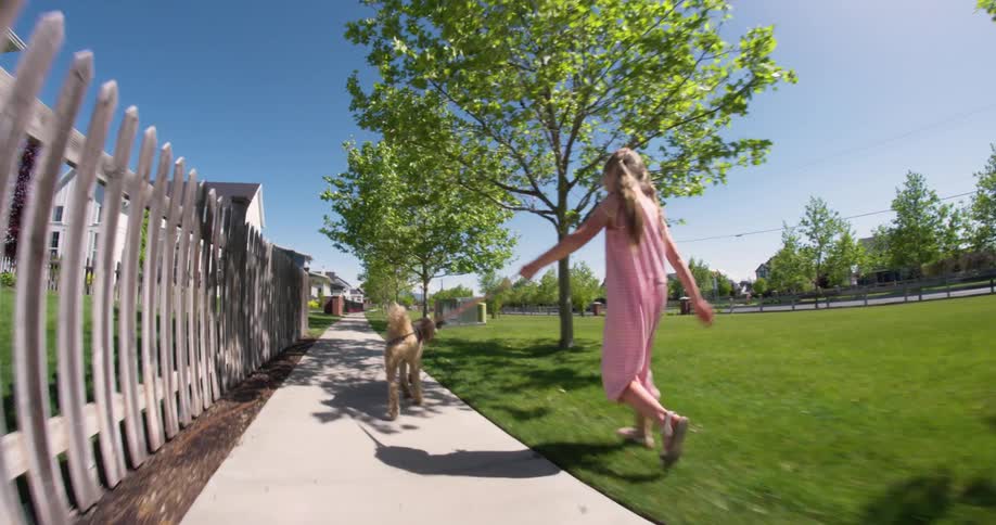 Girl walking on a sidewalk next to some grass with a dog