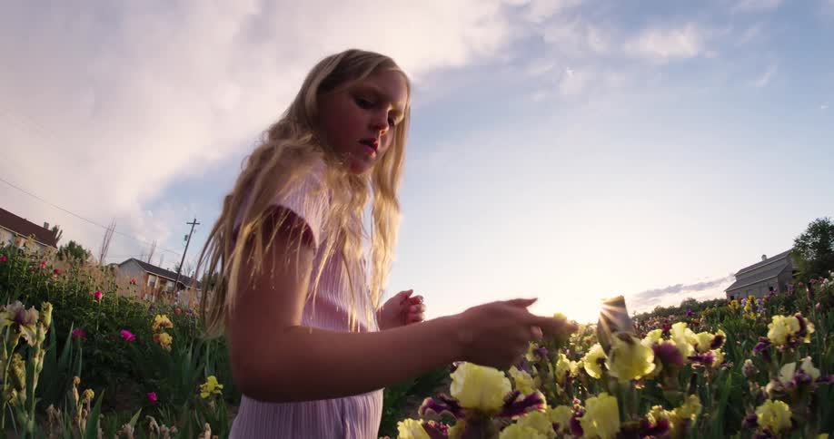 A little blonde girl is in a flower field touching one of the flowers