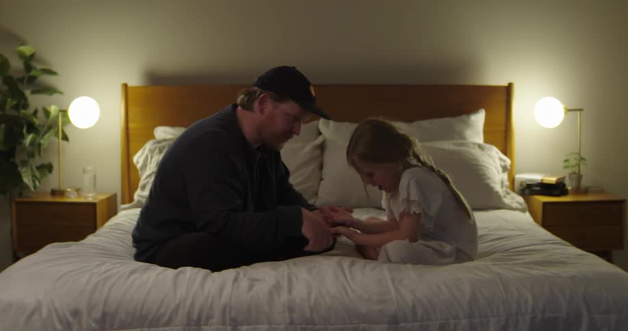 Father sitting on bed with his little daughter playing with her hands