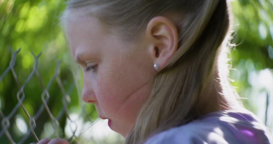 Blonde girl holds her hair while looking through a chain link fence before turning to go