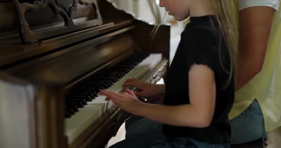 Little blonde girl playing piano next to a woman