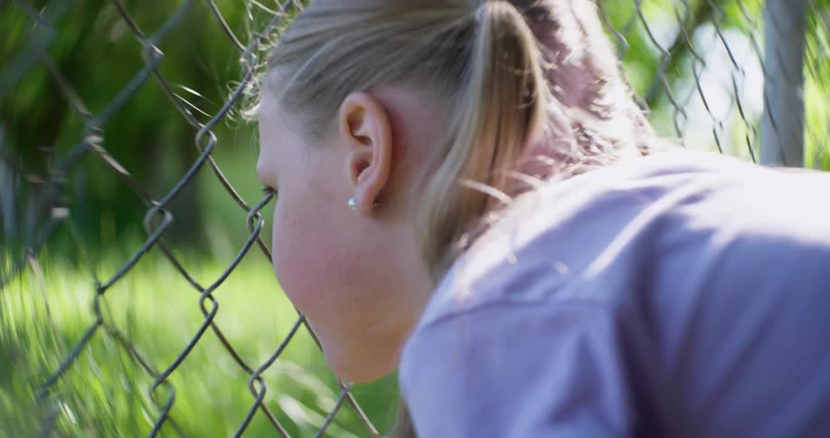 A little girl looking through a chain link fence on a bright sunny day