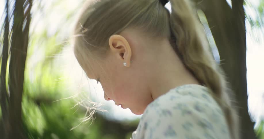 Side portrait of a blonde child in a treelined environment