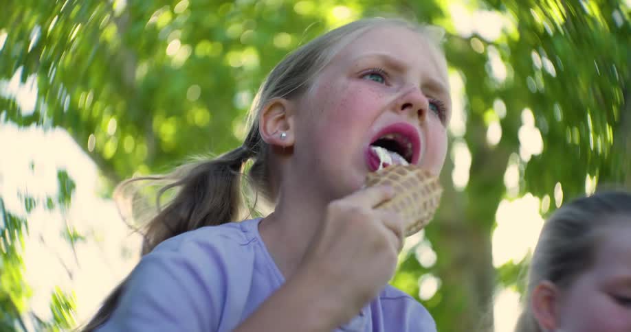Blonde girl sitting next to her twin sister licking her ice cream