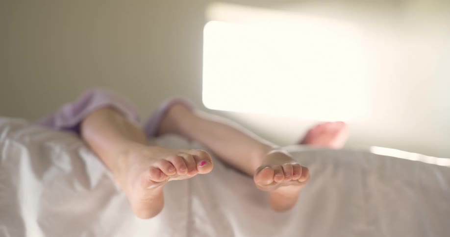 Feet of a little girl lying on the bed with her sister