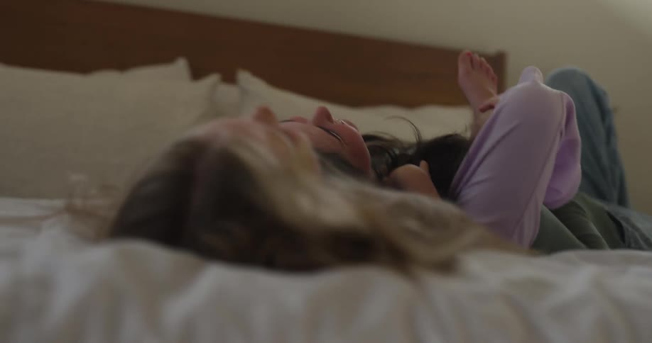 A mother and her daughter fall on the bed while laughing