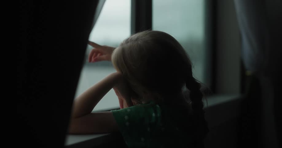 Little blonde girl looking out a rainy window