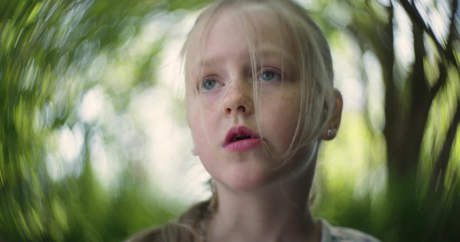 Portrait of a little blonde girl with blue eyes and freckles with trees in the background