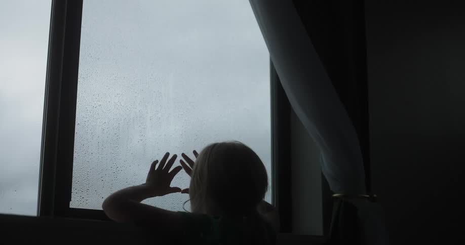 A girl looks out the window at the rain