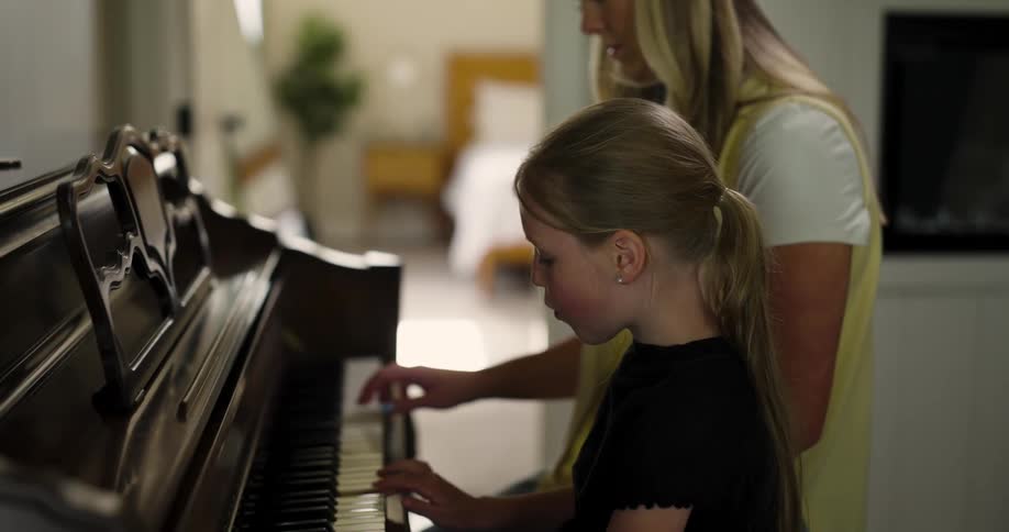 Little blonde girl playing piano next to her mother