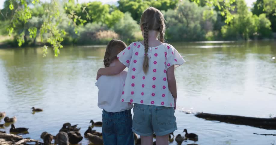 Two girls seen from behind looking at a lake with ducks