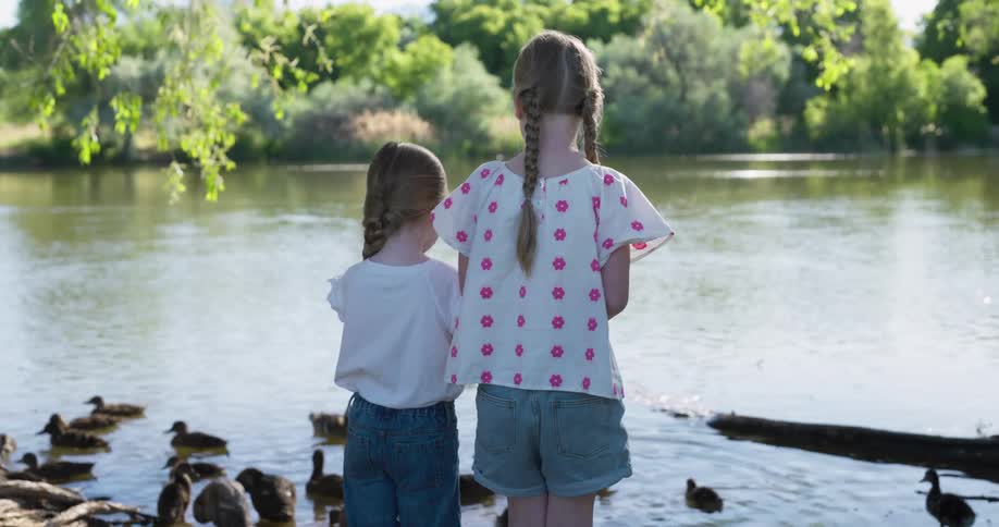Two girls seen from behind watching a lake with ducks