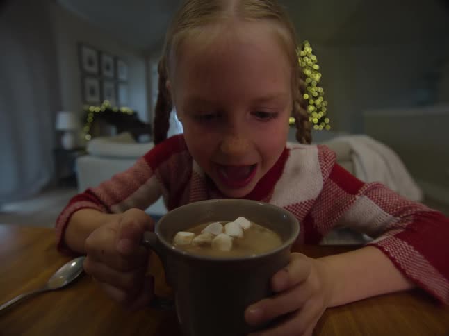 Smiling blonde girl drinks hot chocolate with marshmallows on top