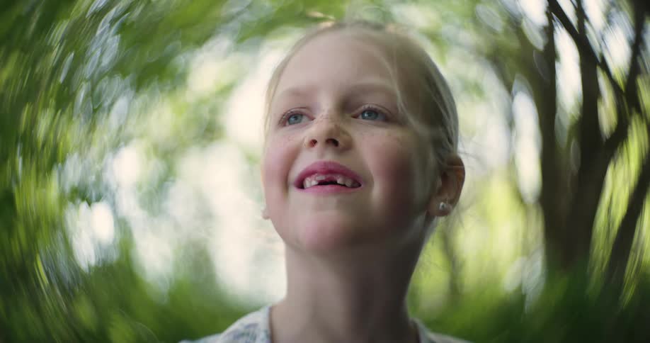 Blonde girl standing outdoors among the trees during summer displays a gap tooth smile and freckles