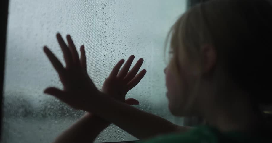Blonde girl with hands passing on the window with raindrops
