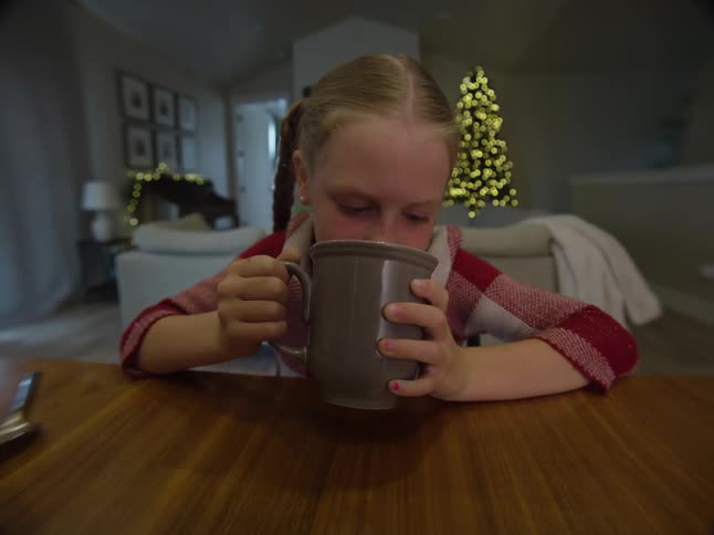 A young girl drinks from a mug while sitting at a table at christmastime