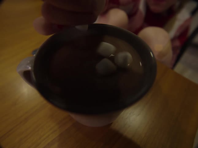 A closeup of a person dropping marshmallows into a cup of hot chocolate