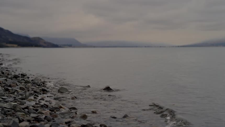 Gentle waves roll onto a rock covered shore on a foggy day