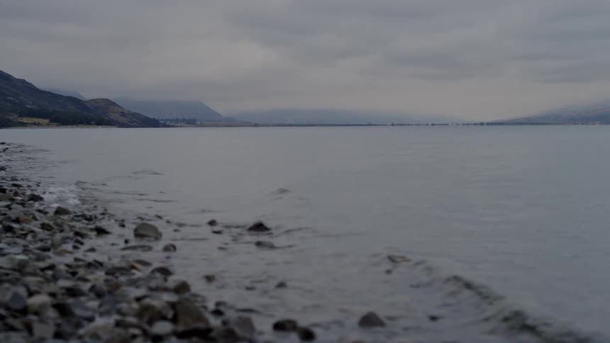 Landscape with calm waters reaching rocks and mountains on the horizon