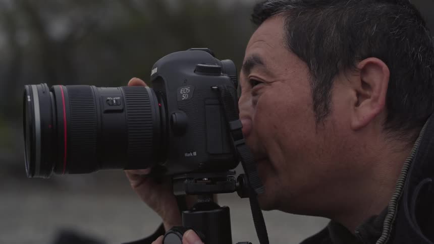 Photographer using a professional camera on a tripod in an outdoor environment and looking into the lens