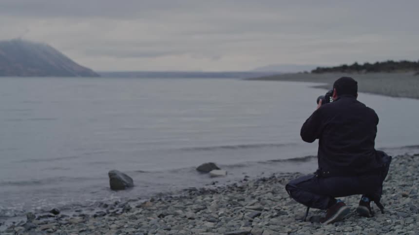 Photographer crouching in front of a lake with mountains in the background