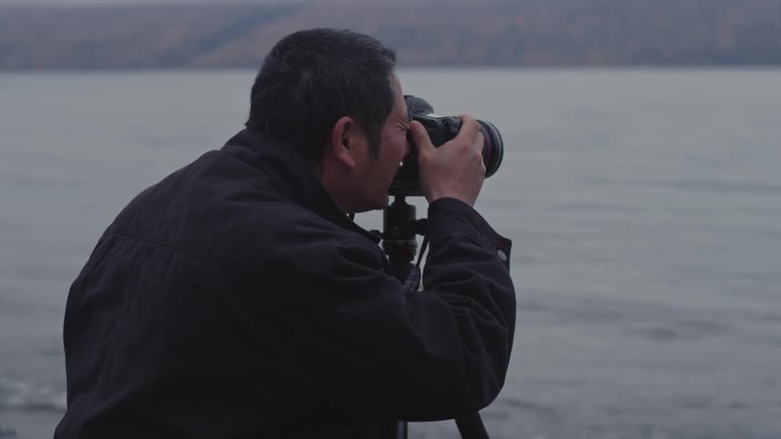 Photographer standing along the coast with his camera on a tripod as he takes pictures