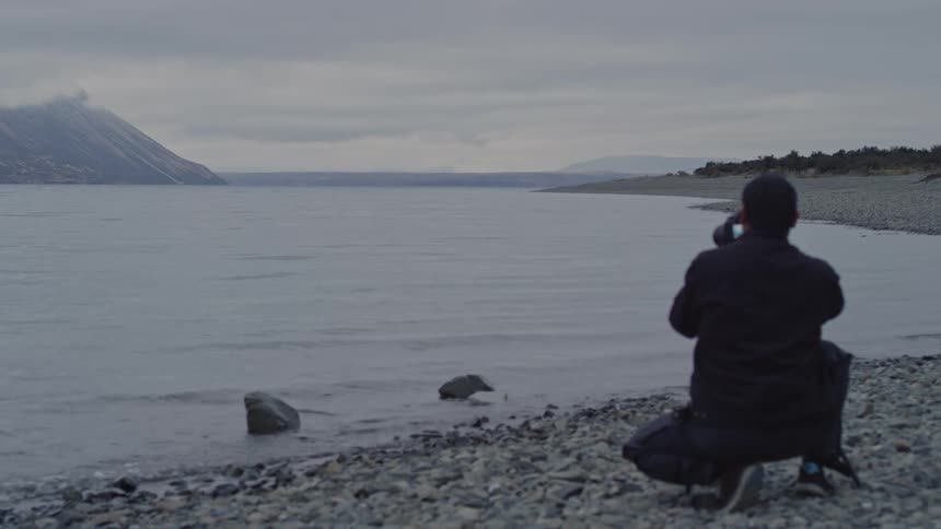 Photographer crouching on the shore takes picture of the landscape using a telephoto lens on a foggy day